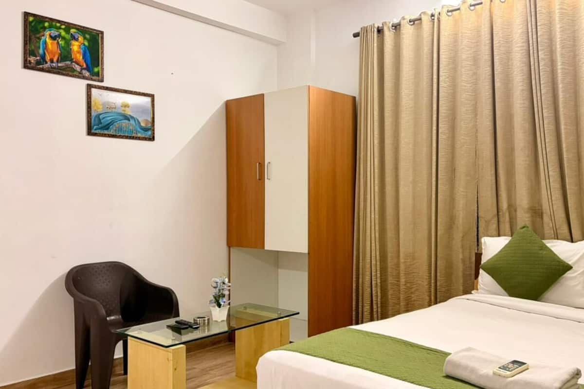 A hotel room with a bed, a desk with a chair, a wardrobe, and two wall art pieces.