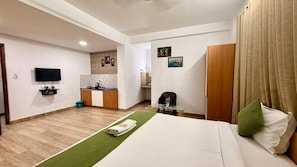 Habitación de hotel con cama, televisor, escritorio y kitchenette.