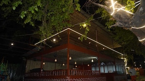 An outdoor covered seating area with brick walls and hanging lights. - Tree Aura Retreat (Rishikesh)