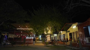 An outdoor area with a pathway leading to a building with a sign that appears to be in a foreign language. - Tree Aura Retreat (Rishikesh)