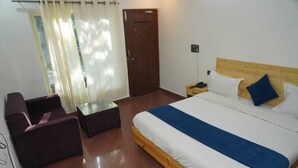 A hotel room with a bed, a small table, a chair, and a wooden door. - Tree Aura Retreat (Rishikesh)