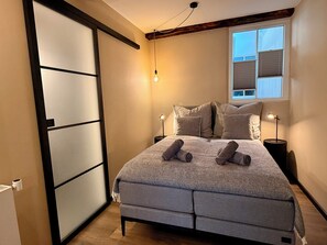 Ein Schlafzimmer mit einem Bett, zwei Nachttischlampen, einem Fenster mit Jalousien und einer Schiebetür.