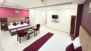 A modern hotel room with a large bed, a desk, a chair, a television, and a ceiling fan. - Hotel Excotia Haridwar (Haridwar)