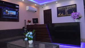 A reception area with a flat-screen TV, a guitar, a vase of flowers, and a painting on the wall. - Hotel Excotia Haridwar (Haridwar)