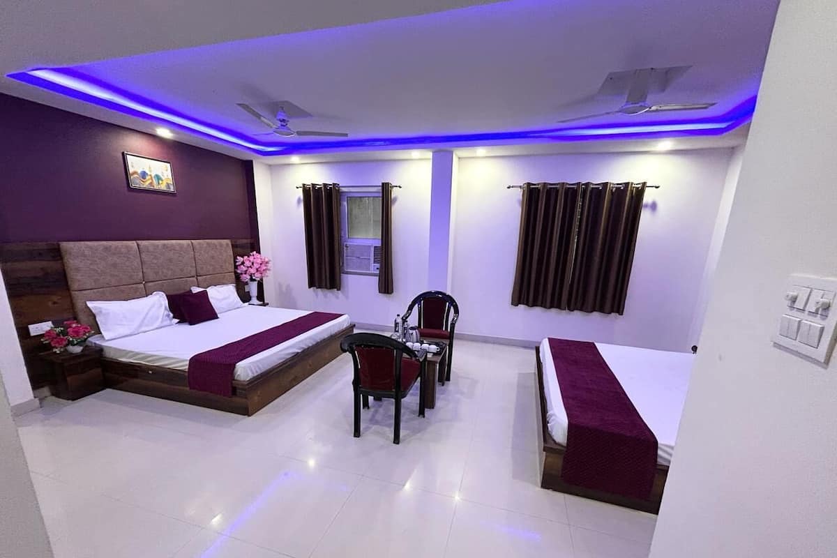 A hotel room with two beds, a desk, a chair, a small table, a window with curtains, and a ceiling fan.
