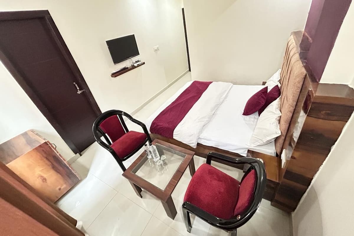 A room with a bed, two red chairs, a small table, a TV, and a wooden cabinet.