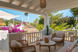 A covered outdoor seating area with wicker furniture, a round table, and a potted cactus. - Villa Lantana with private pool - My Rental Homes (Santa Eulària Des Riu)