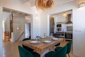 A dining area with a wooden table set for four, surrounded by green chairs, a kitchen with modern appliances, and a staircase leading to another level. - Villa Lantana with private pool - My Rental Homes (Santa Eulària Des Riu)
