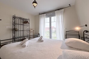 Ein Schlafzimmer mit einem Bett, einem Metallregal, einem Fenster mit Vorhängen und einer Pendelleuchte.
