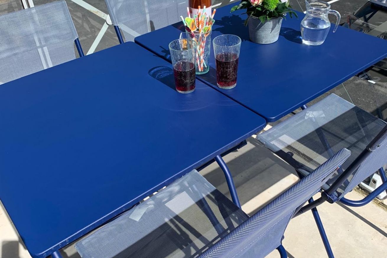 A blue outdoor table with two glasses of dark liquid, a pitcher, and a striped straw cup.