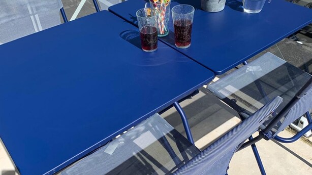 Mesa azul al aire libre con dos vasos de líquido oscuro, una jarra y un vaso con pajita a rayas.