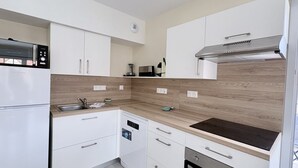 A modern kitchen with white cabinetry, a built-in oven, a microwave, and a stainless steel range hood. - Chuchotis, apartment for 4 with balcony and parking space (LE Crotoy)