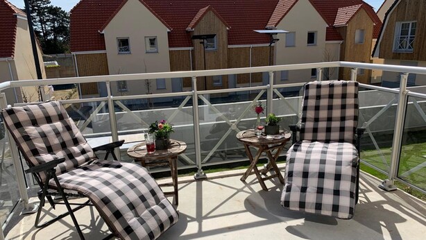 A balcony with two checkered lounge chairs, a small round table with a vase of flowers, and a view of neighboring houses. - Chuchotis, apartment for 4 with balcony and parking space (LE Crotoy)
