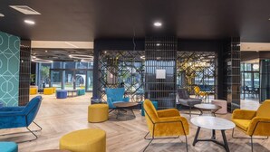 A modern lounge area with wooden flooring, blue and yellow chairs, and round tables. - Student Only Onyx (Birmingham)