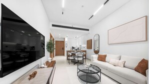 Ein modernes Wohnzimmer mit großem Flachbildfernseher, einem Essbereich mit Tisch und Stühlen, einer Couch mit Kissen und einem großen abstrakten Gemälde an der Wand.