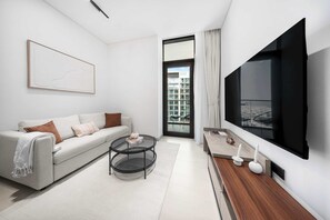 A modern living room with a sofa, coffee table, TV, and a large window. - StayShort - Charming 1BR Retreat in JVC Sleeps 4 (JVC)