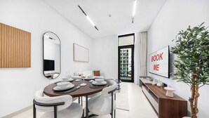 Ein moderner Essbereich mit einem runden Tisch, weißen Stühlen, einer Holzwand, einem Spiegel, einem Fernseher und einer Zimmerpflanze.