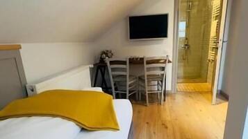 Un dormitorio con una cama, un escritorio, una silla y una televisión montada en la pared.
