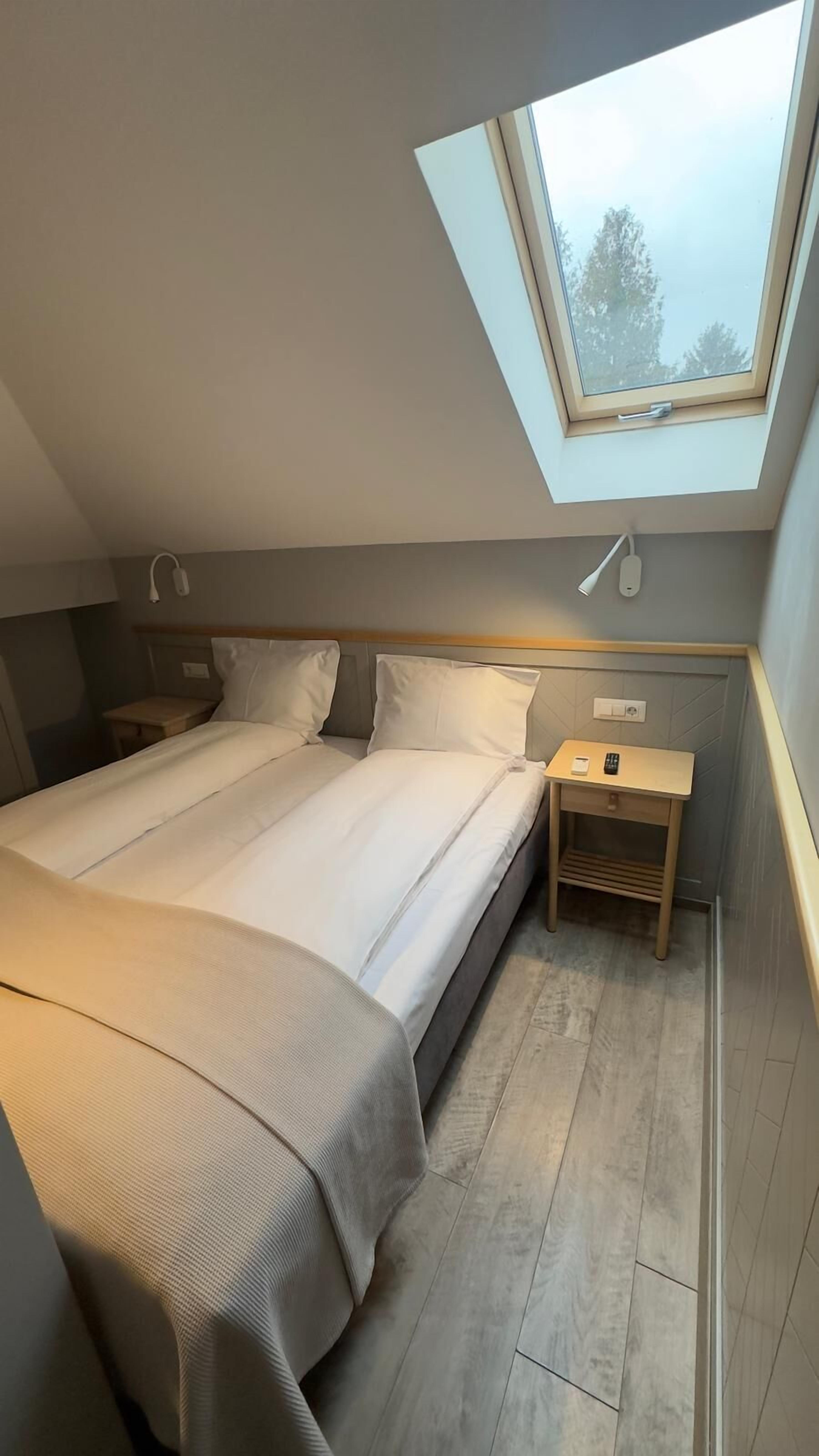 A bedroom with a skylight, a bed, bedside tables, and a small wooden nightstand.