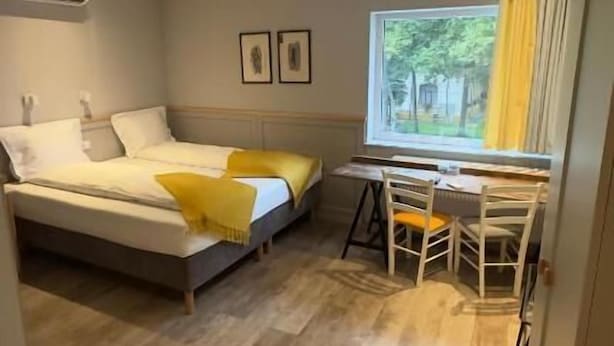 A bedroom with a bed, a desk, and a chair. There is a window with curtains, a picture on the wall, and an air conditioning unit. - Villa Piazzetta (Bacău)