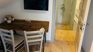 A room with a wooden dining table, chairs, a flat-screen TV, and a glass-enclosed shower area. - Villa Piazzetta (Bacău)