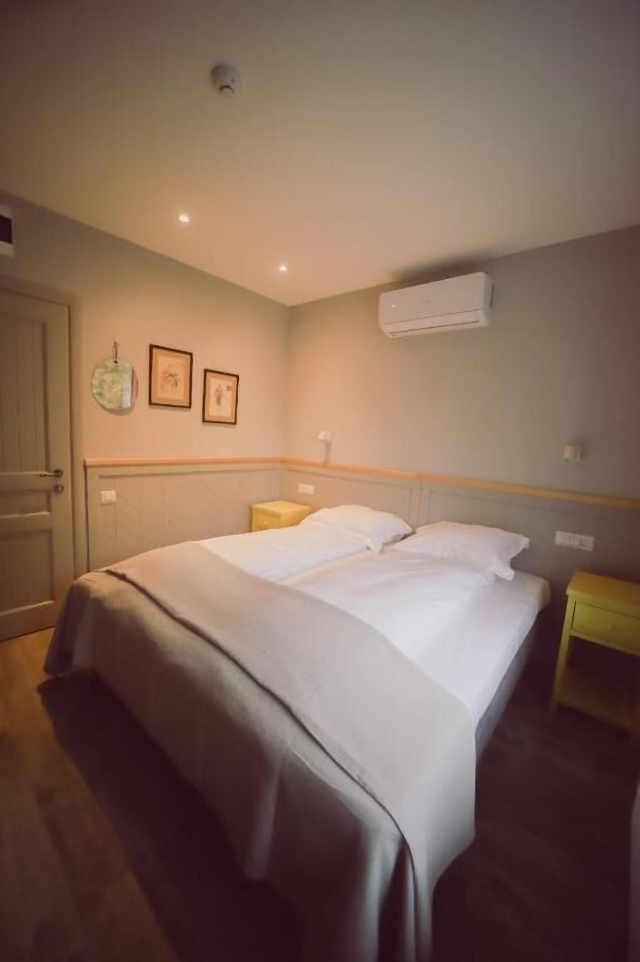 A hotel room with a bed, bedside tables, a door, and a wall-mounted air conditioner.