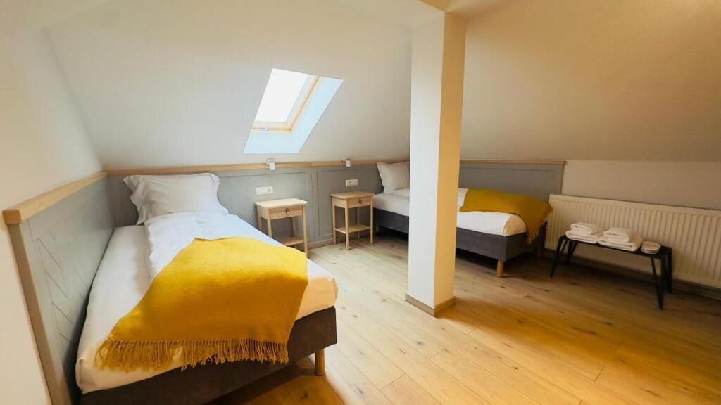 Una habitación con cama, una mesita, una silla, un radiador y un tragaluz.