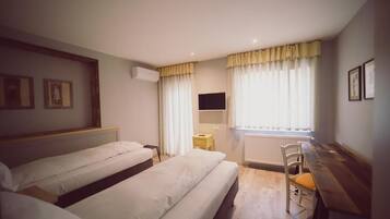 A room with two beds, a desk, a chair, a radiator, and a TV on the wall.