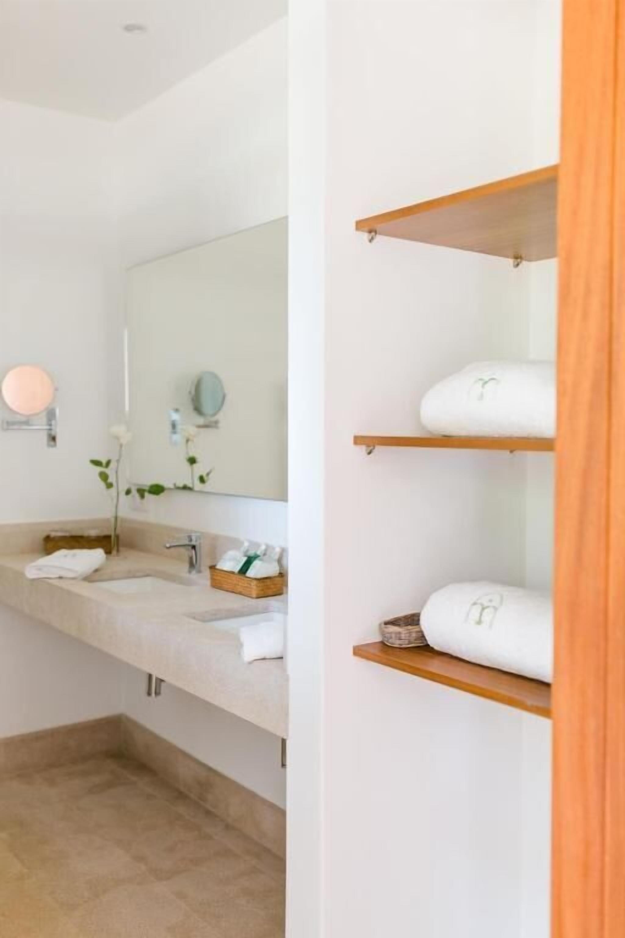 A modern bathroom with a large mirror, two sinks, and shelves with towels.