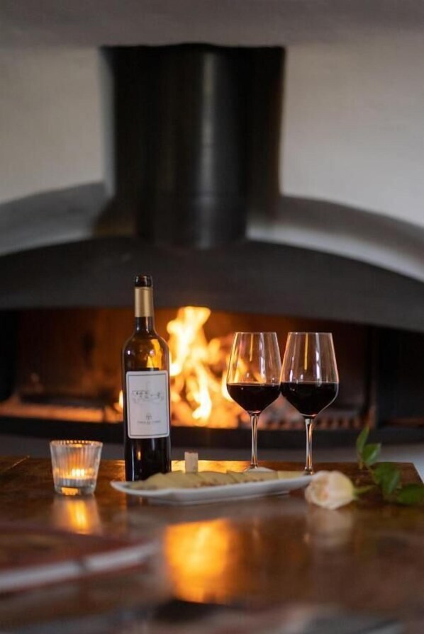 A table with a bottle of wine, two glasses of red wine, and a candle, set against a backdrop of a wood-burning pizza oven. - Finca Es Cabàs (Santa Maria del Camí)