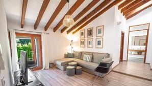 A modern living room with a sofa, coffee table, and chairs, wooden beams on the ceiling, and framed pictures on the wall. - Finca Es Cabàs (Santa Maria del Camí)