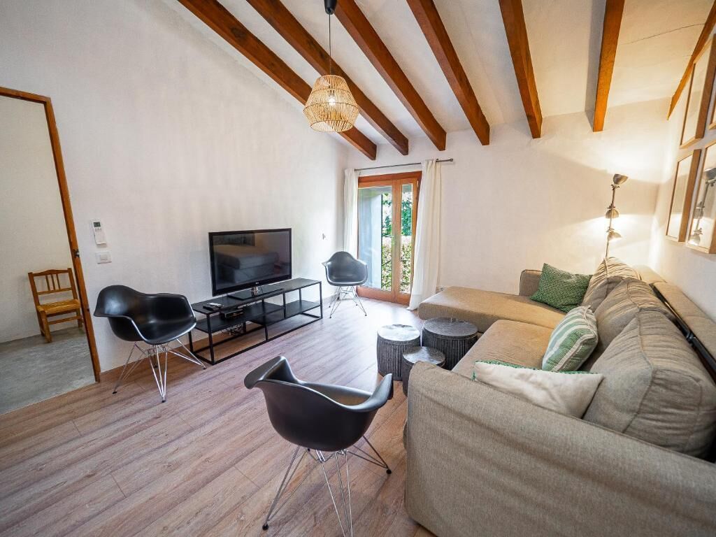 Una sala de estar con sofá, sillas, televisor, vigas de madera y una ventana.