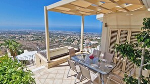 An outdoor patio with a table and chairs, overlooking a coastal cityscape. - Breathtaking Villa, Panoramic Sea View, Infinity Pool, 3BDR (Tala)