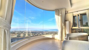 Un balcon doté d’une paroi en verre incurvé, d’un canapé et de rideaux.