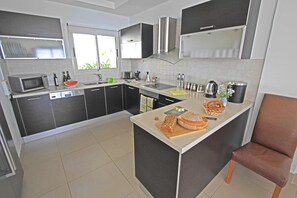 A modern kitchen with dark cabinets, a microwave, a toaster, and a large island with bread and a cutting board. - Breathtaking Villa, Panoramic Sea View, Infinity Pool, 3BDR (Tala)