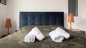 A neatly made bed with two rolled towels, a dark headboard, a window with blinds, a lamp, and a framed picture on the wall. - Special Launch Price! Amazing Sea View 1BR Villa, Garden & Gym (Polis Chrysochous)