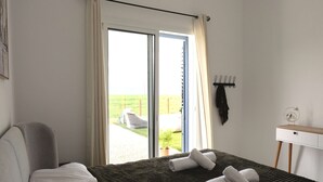 Una camera da letto con un letto, un comodino, una sedia, una finestra con tende e vista sull'esterno.