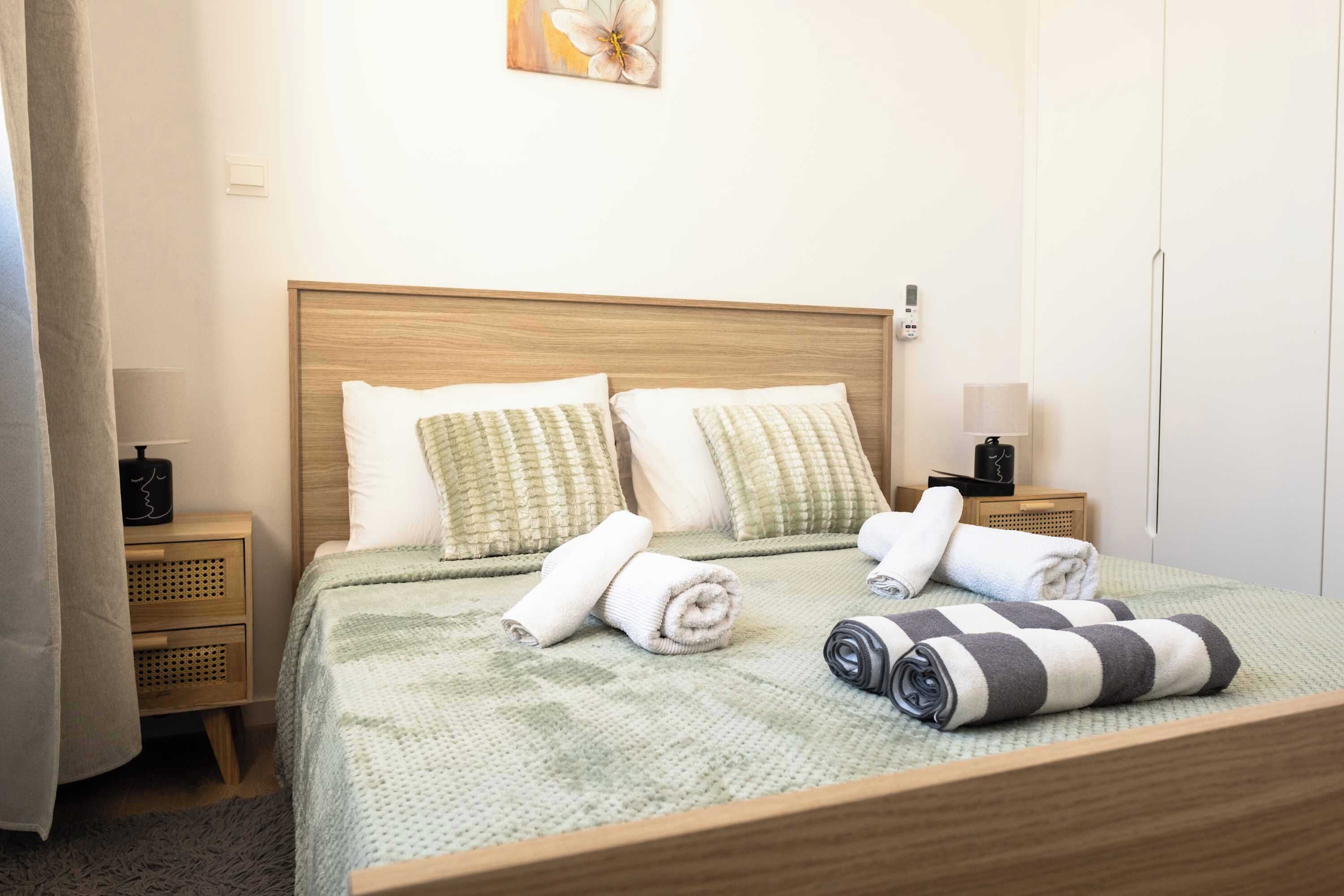 Un lit bien fait, avec des oreillers et des serviettes enroulées, une table de chevet avec une lampe et un interrupteur fixé au mur.