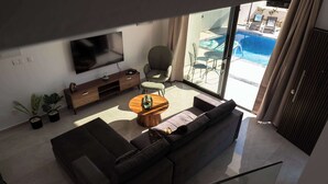 Ein modernes Wohnzimmer mit einer Couch, einem Couchtisch, einem Fernseher und Blick auf einen Swimmingpool.