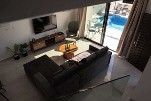 Ein modernes Wohnzimmer mit einer Couch, einem Couchtisch, einem Fernseher und Blick auf einen Swimmingpool.