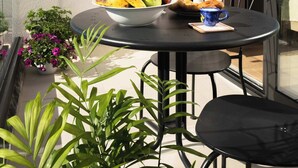 Ein Balkon mit rundem Tisch, Stühlen, einer Fruchtschale, einer Flasche und einem Blumentopf.