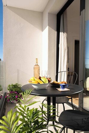 Ein Balkon mit rundem Tisch, Stühlen, einer Fruchtschale, einer Flasche und einem Blumentopf.