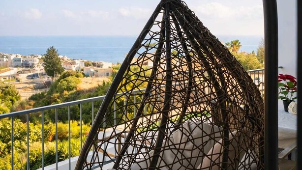 Una silla colgante en un balcón con vista al mar y edificios.