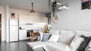 Una cocina moderna con armarios blancos, una zona de comedor con mesa de madera y un sofá gris con cojines decorativos.