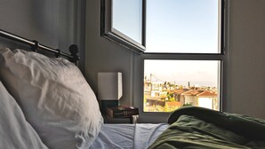 Un dormitorio con cama, una mesita de noche con lámpara y ventana que ofrece vista a la ciudad.