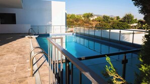 Una piscina con barrera de vidrio, baranda metálica y vista despejada del paisaje circundante.