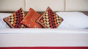 Uma cama com lençóis brancos, duas almofadas estampadas e um cobre-leito vermelho.