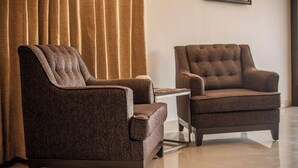 Duas poltronas com design estofado, uma mesa pequena e uma cortina em um quarto com piso de azulejos.