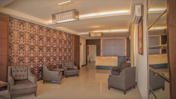 Um saguão de hotel com balcão de recepção, várias poltronas, parede estampada e um lustre moderno.