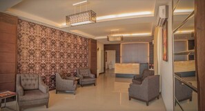 Un vestíbulo de hotel con una recepción, varios sillones, un papel tapiz con diseño y una lámpara de araña moderna.